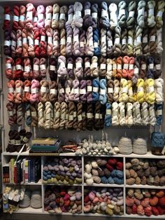 many skeins of yarn are on display in a storage area with white shelving