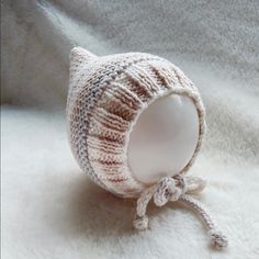 a knitted hat with a white ball attached to the side on a white blanket