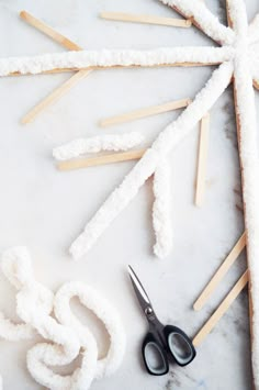 scissors, sticks and yarn are sitting on a white surface next to snowflakes