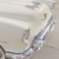 an old white car parked on the side of the road with chrome trimmings