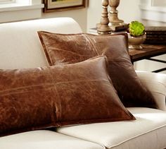 two brown leather pillows sitting on top of a white couch next to a wooden table