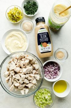 ingredients to make chicken salad laid out on a white counter top, including onions, celery, carrots and mayo