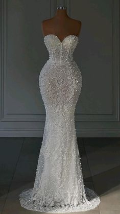 a white wedding dress on display in front of a gray wall and wooden mannequin