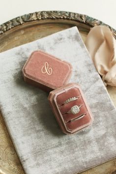 two pink velvet jewelry boxes sitting on top of a silver tray next to a napkin