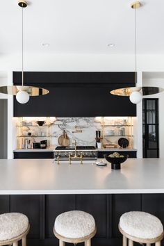 a kitchen with marble counter tops and stools in front of an island that has gold lights hanging from the ceiling