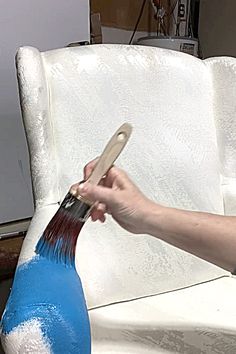 a person is painting a white chair with blue paint and a wooden brush in it