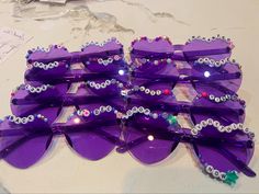 several purple sunglasses with jewels on them sitting on a white table top next to other items