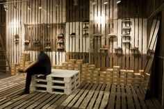 a man sitting on top of a wooden crate in a room filled with shelves and ladders