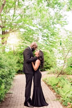 a man and woman standing next to each other on a brick path in the woods