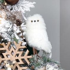 a white owl sitting on top of a christmas tree next to snowflakes and ornaments