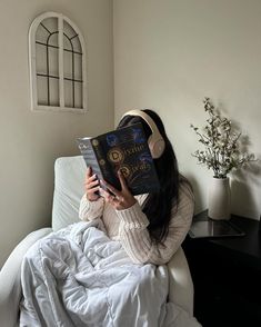 a woman sitting in bed with headphones on reading a book