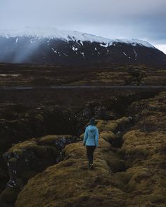 a woman standing on top of a lush green field next to a snow covered mountain