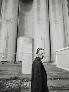 black and white photograph of man in front of grain silos, looking at camera