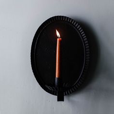 a lit candle on a black plate with a white wall in the backround