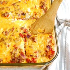 a casserole dish with meat and cheese in it on a white towel next to a wooden spoon