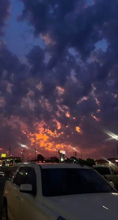 cars parked in a parking lot at night with the sun setting behind them and clouds