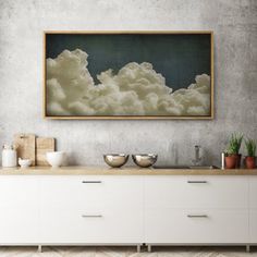 a painting hanging on the wall above a white dresser with bowls and cups in front of it