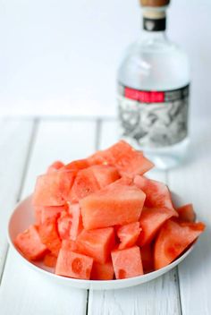 watermelon cubes on a white plate next to a bottle