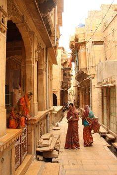 three women in sari walking down an alleyway with stone buildings on either side