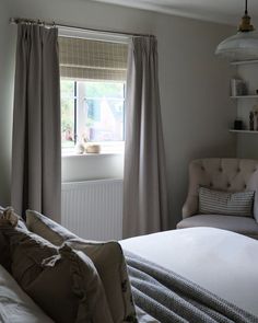 a bed sitting under a window next to a white chair with pillows on top of it