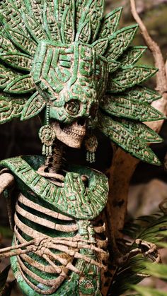 a green skeleton statue sitting on top of a tree branch next to a leafy plant