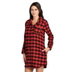 a woman wearing a red and black plaid shirt dress with long sleeves, standing in front of a white background