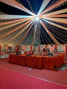 the inside of a tent decorated with orange and white linens is lit up at night