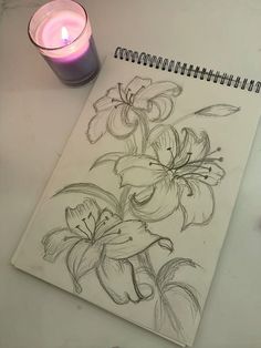 a pencil drawing of flowers next to a lit candle on a white table with a pen