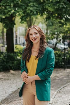 a woman is standing in front of some trees and smiling at the camera with her hands on her hips