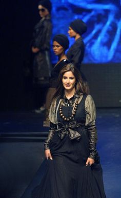 a woman walking down a runway wearing a black dress