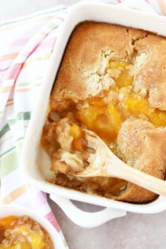 a casserole dish filled with peach cobbler and topped with a wooden spoon