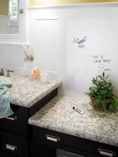 two sinks in a bathroom with writing on the wall above them and a potted plant next to it