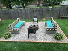 an outdoor seating area with blue cushions on the benches and gravel in the middle, surrounded by green grass