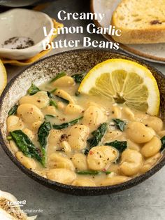 creamy lemon garlic butter beans in a bowl with sliced lemons and bread on the side