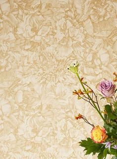 a vase filled with different colored flowers on top of a wooden table next to a wall