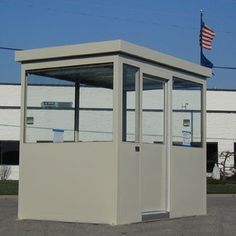 a small white building sitting in the middle of a parking lot next to an american flag