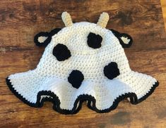 a crocheted cow hat is sitting on a wooden surface with black and white spots