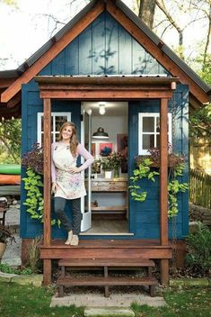 a woman standing in the doorway of a small blue shed with plants growing on it