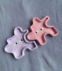 two small clay animals sitting on top of a blue surface next to each other, one pink and the other purple