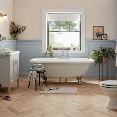 a white bath tub sitting next to a toilet in a bathroom under a large window