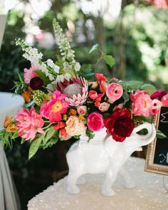 an elephant vase filled with colorful flowers on top of a table next to a chalkboard