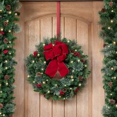 a christmas wreath with red bow hanging on a wooden door surrounded by evergreen and pine cones