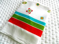 the folded towel is on top of the white bed sheet with colorful stripes and flower designs