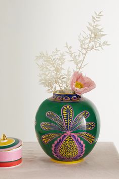 a green vase with flowers in it sitting on a table next to a pink container