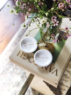 two white bowls sitting on top of a wooden table next to a vase filled with flowers