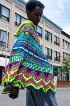 a young man wearing a colorful shawl standing in front of a tall brick building