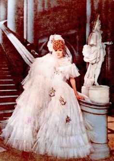 an old fashion photo of a woman in a white dress sitting on some steps next to a statue