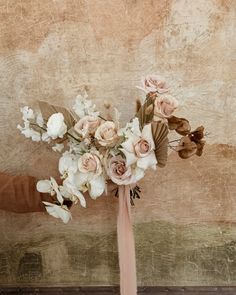 a person holding a bouquet of flowers in front of a brown wall with peeling paint