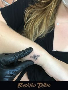 a woman with a bee tattoo on her left arm and black gloves is sitting down