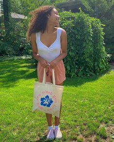 a woman standing in the grass holding a bag